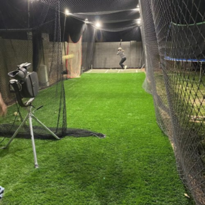 A baseball player training in a backyard batting cage with lights